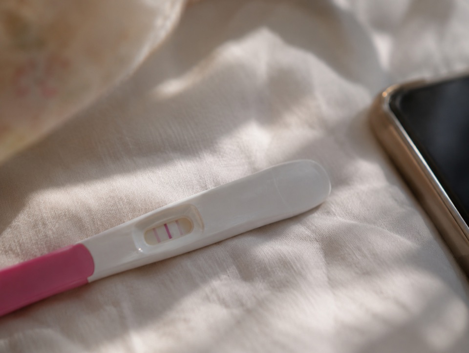 임신 테스트기를 손에 들고 휴대폰으로 산부인과 예약을 알아보는 여성